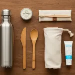 Overhead flat lay of eco-friendly travel essentials on a wooden surface - reusable water bottle, bamboo utensils, cloth bags, and a passport